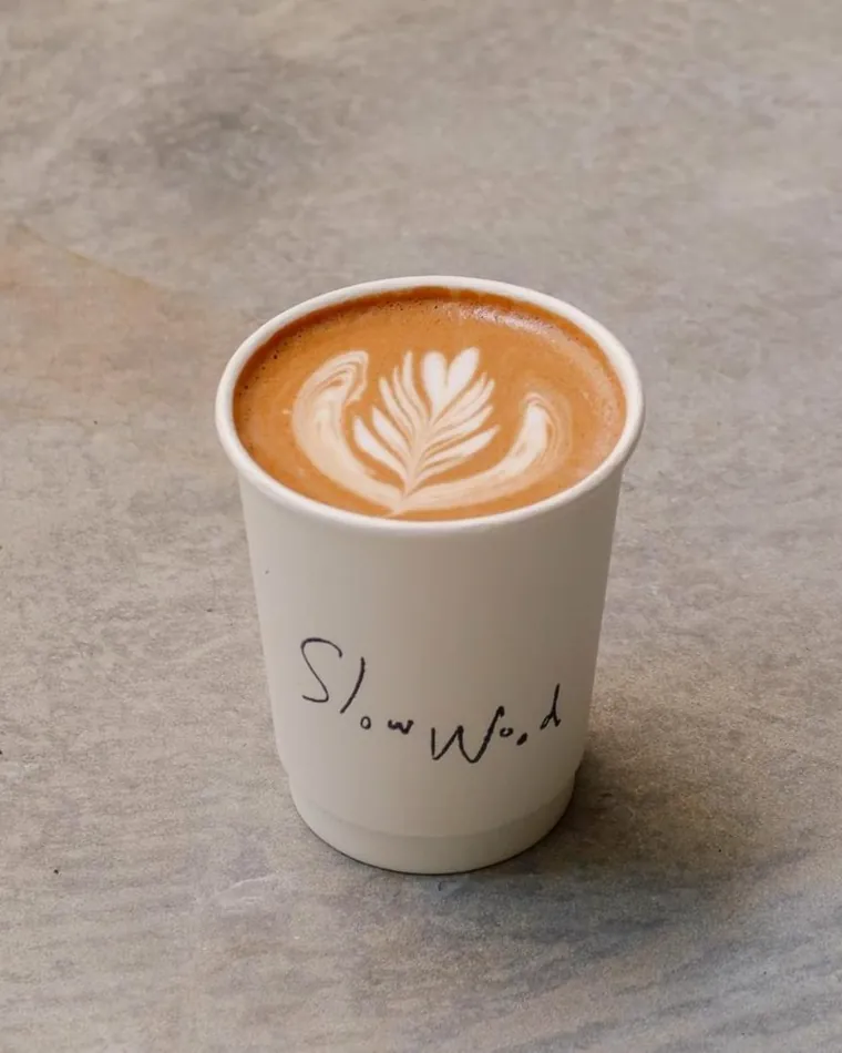 A latte in a Slow Wood cup, latte art on top.