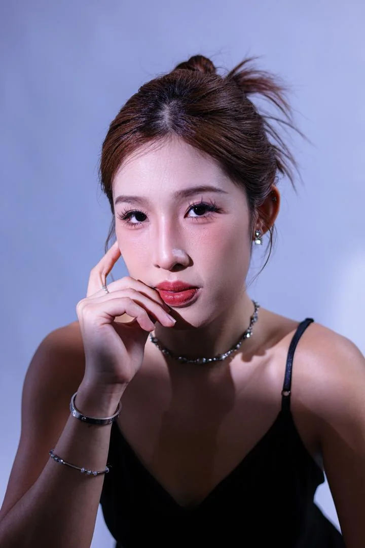 Crystal Lai in a studio portrait, one hand to her face.
