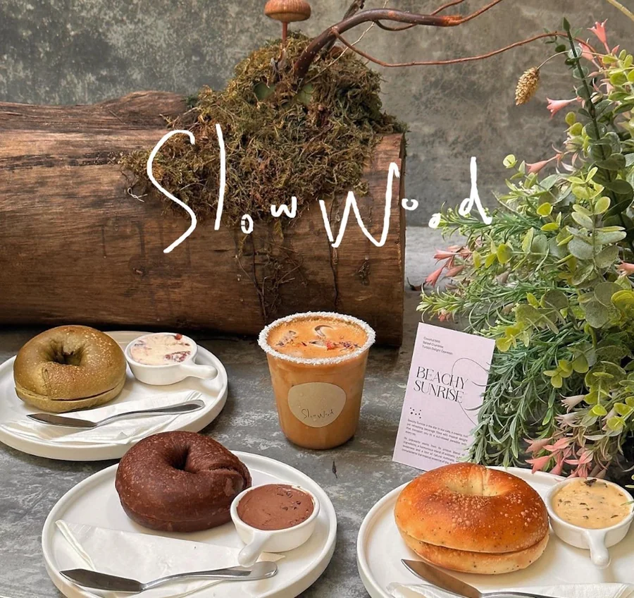 Slow Wood's bagels, pastries and drinks laid out in front of a merbau log.
